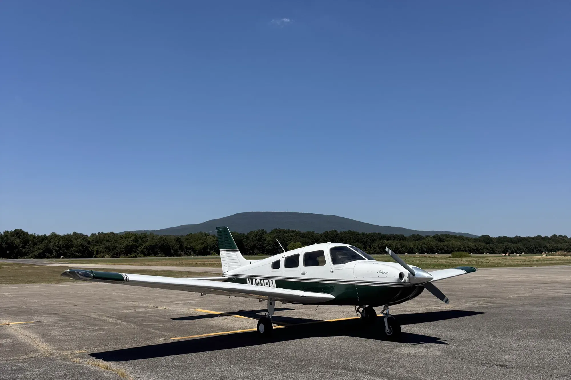 N431RM, a white Piper Archer III with dark green and gold trim, parked on an airport ramp under a clear blue sky.