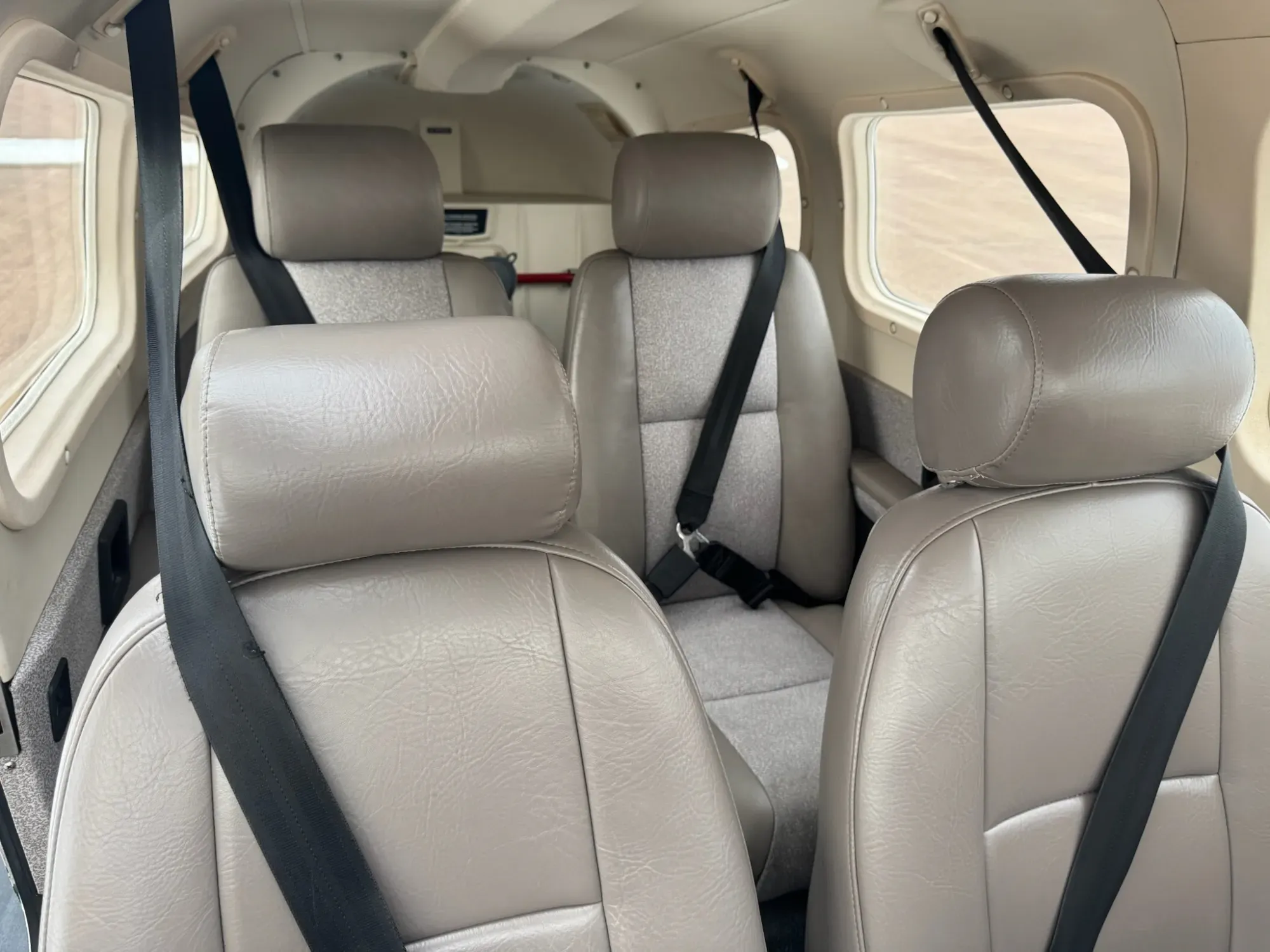 Cabin looking aft from the front, with the front seats in the foreground and the rear seats behind them, all in tan leather with gray fabric inserts.