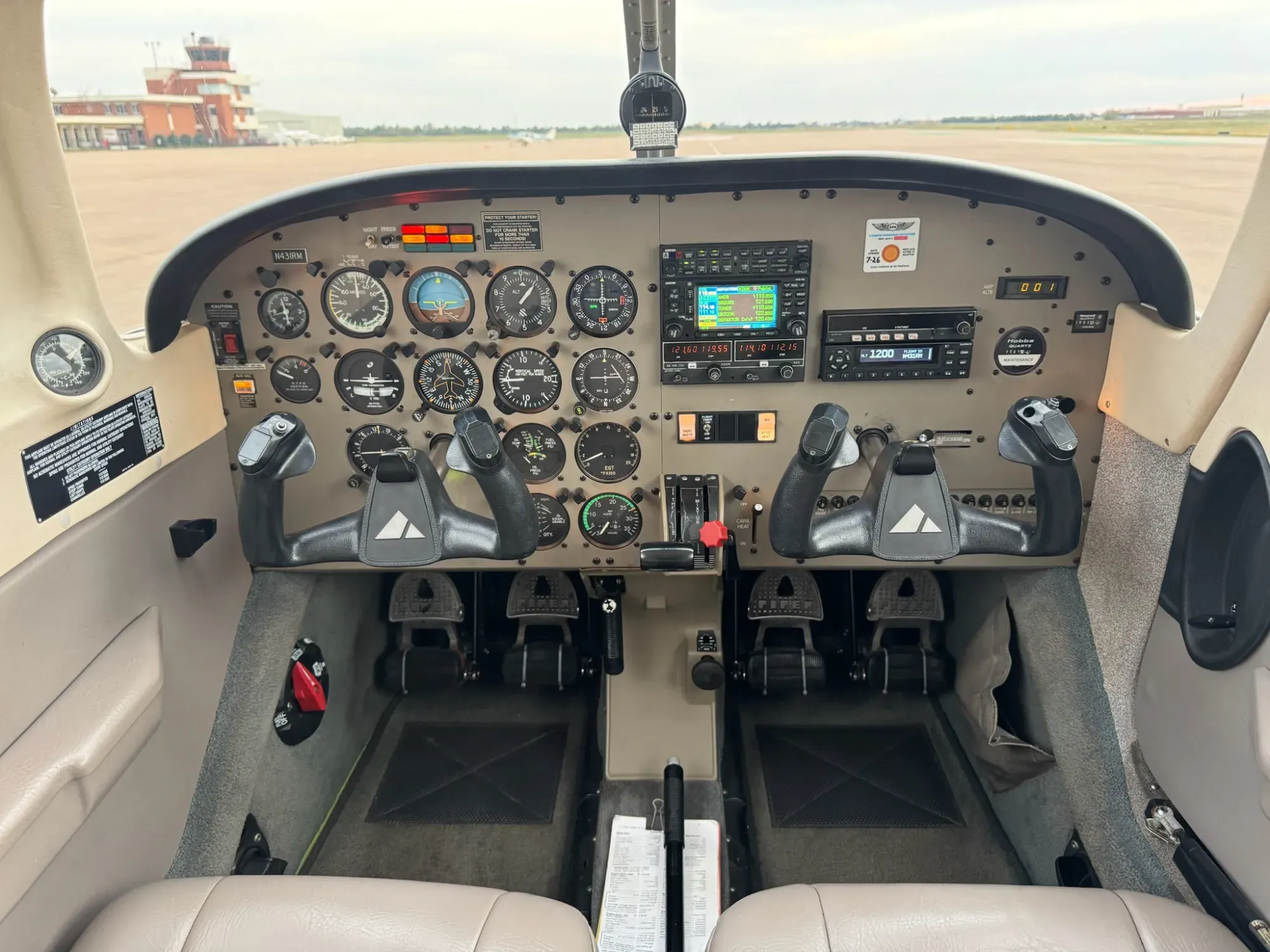 Instrument panel and dual control yokes seen from behind the front seats, with the airport control tower visible through the windshield.