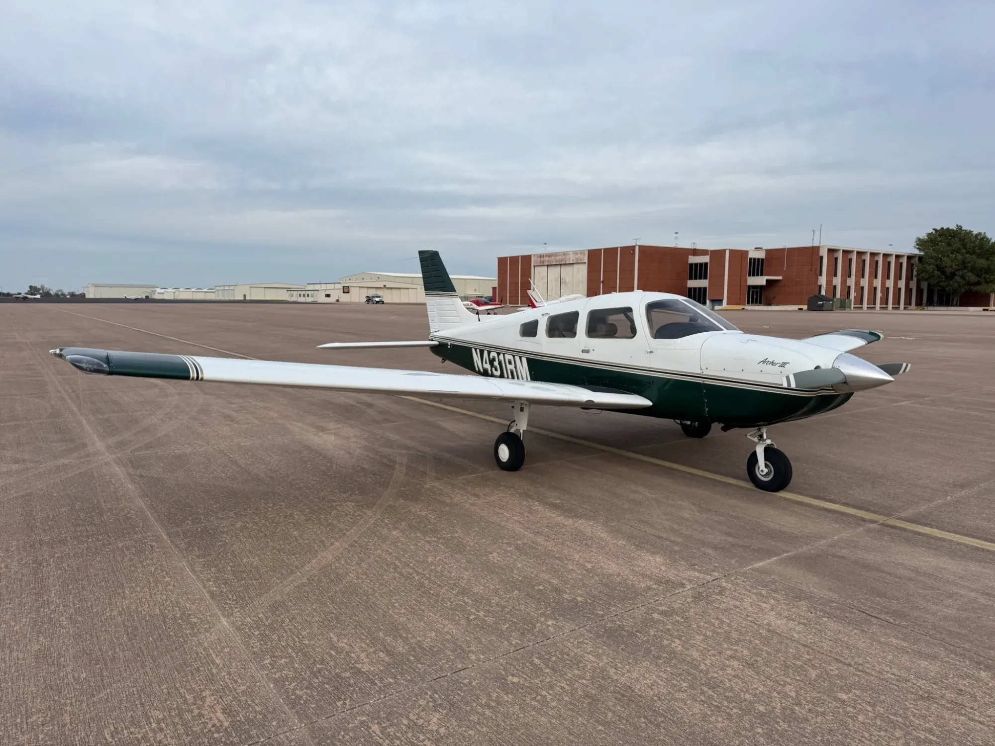 N431RM parked on a concrete ramp, seen from the front right, showing the white paint with dark green and gold trim, the Archer III script on the cowling and the registration on the fuselage.
