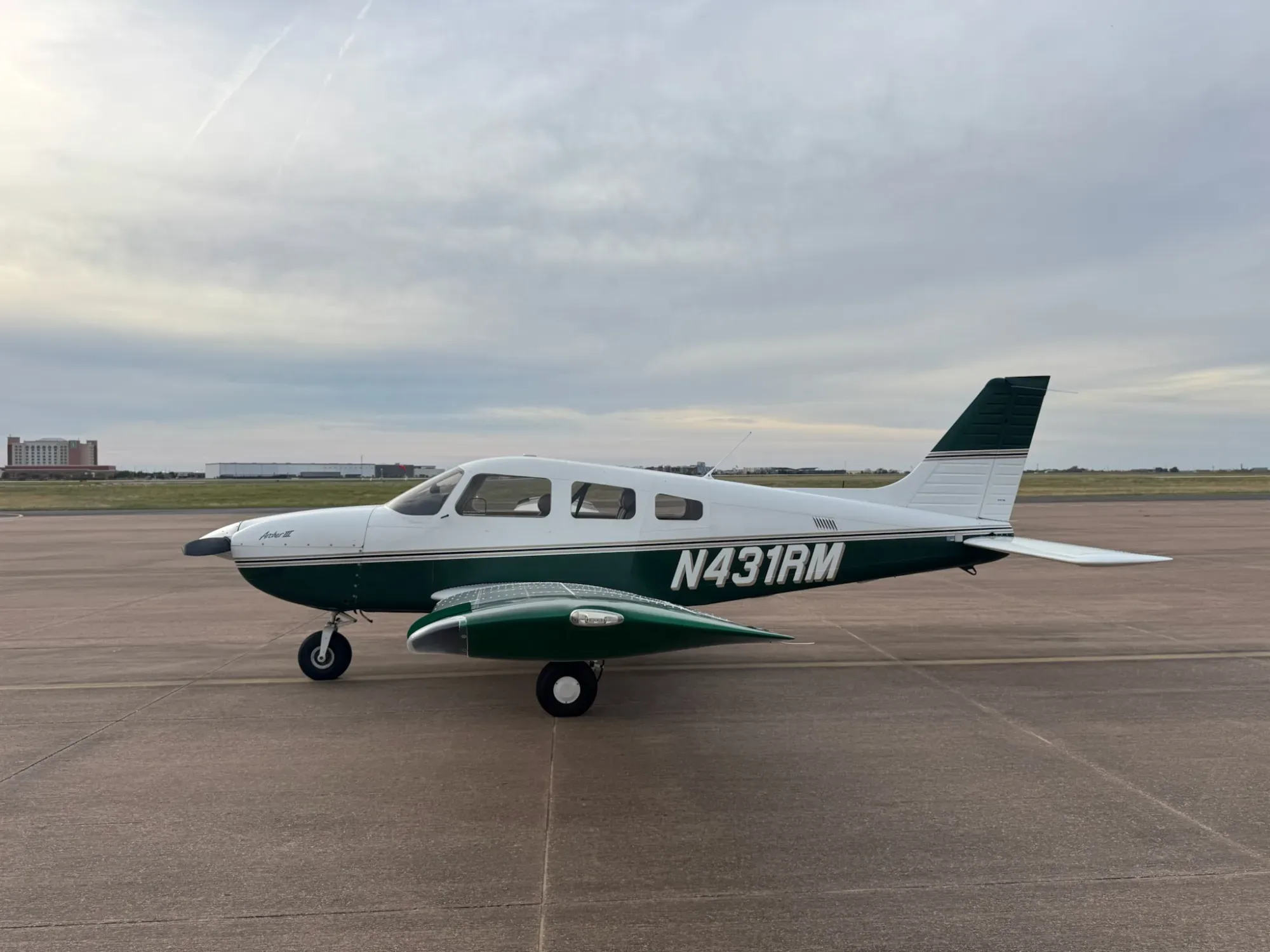 Left side profile of N431RM on the ramp, showing the full length of the fuselage, the green and gold stripes and the registration.