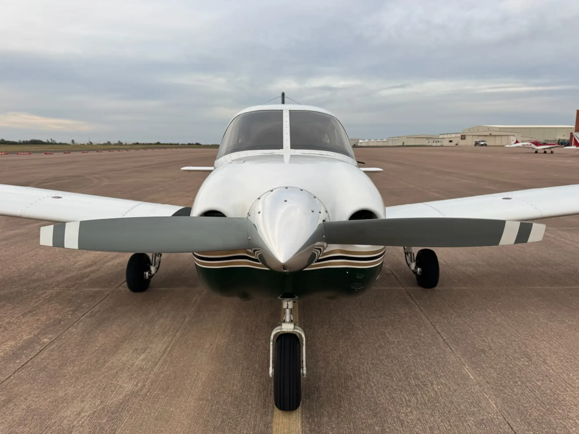 Close view of the nose of N431RM, with the polished spinner, the two-blade propeller, the green and gold cowling stripes and the nose gear.