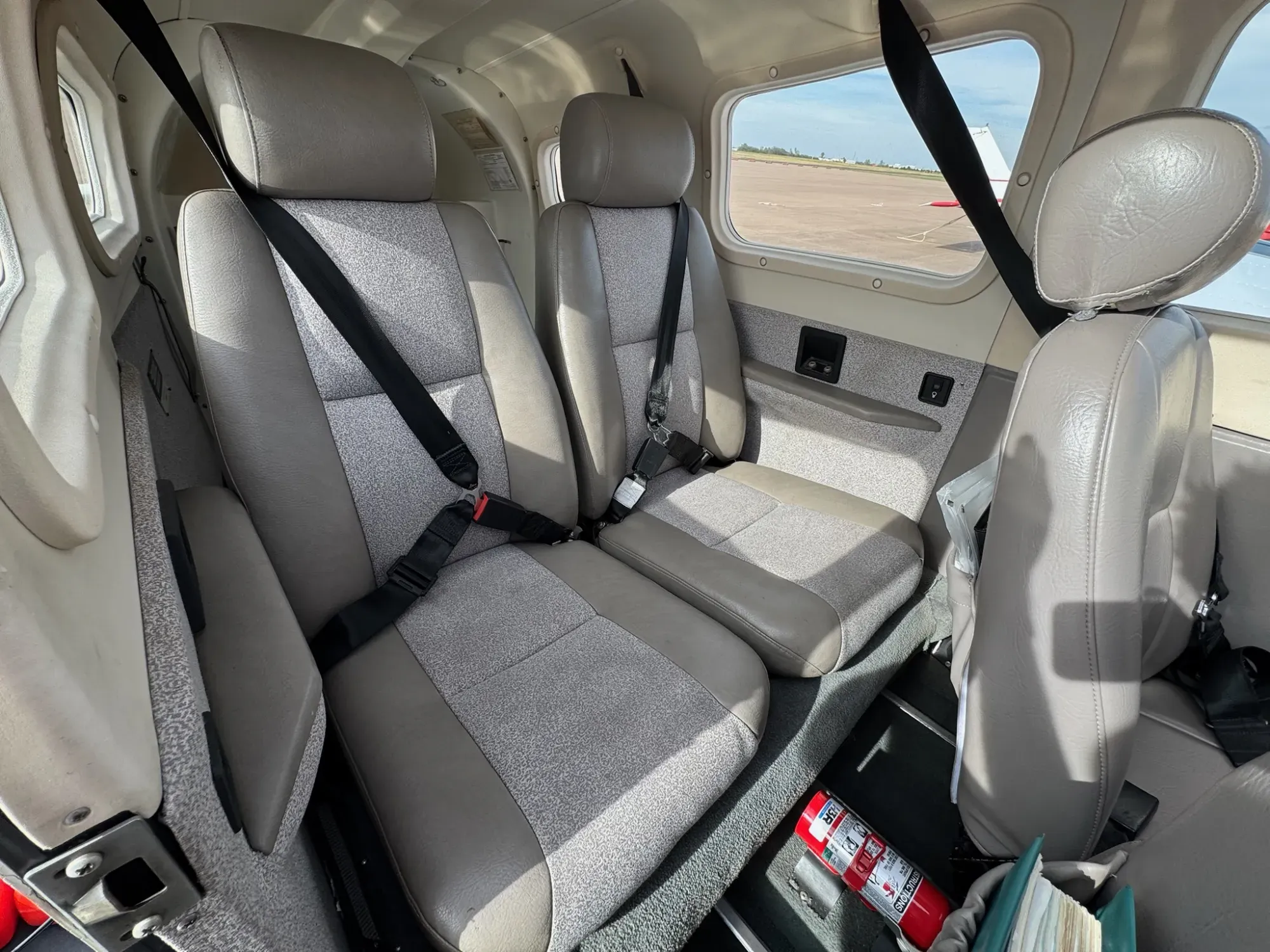 The two rear seats in tan leather with gray fabric inserts, each with a lap belt and shoulder harness.
