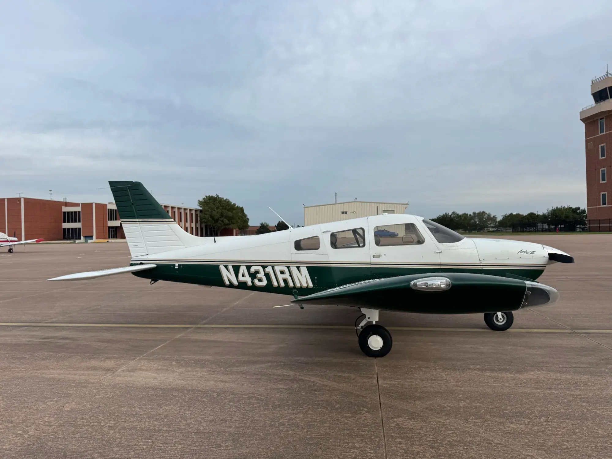 Right side of N431RM on the ramp, with the cabin door, the green lower fuselage and the N431RM registration, and the airport control tower in the background.